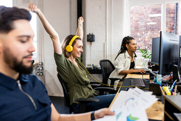 Happy businesswoman wearing headphones sitting in front of desktop at office
