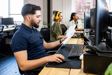 Young businessman using desktop and holding charts in office