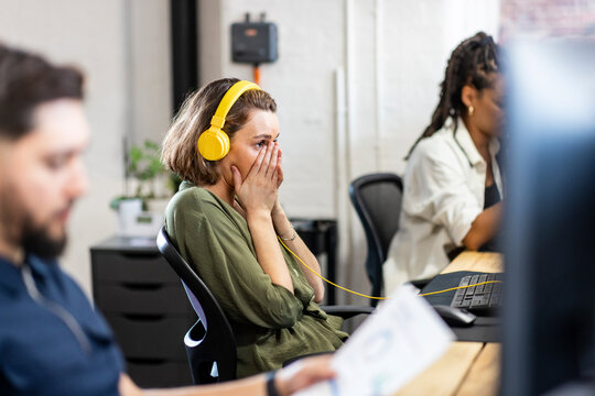 Businesswoman wearing headphones sitting in front of desktop at office
