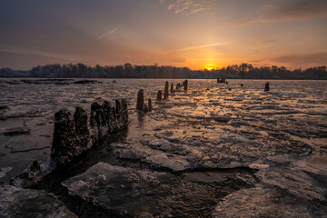 Remains of an old pier over a frozen river during a beautiful sunrise
