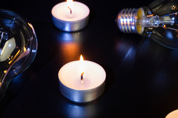 Electric lamp and candle on a dark background. Incandescent lamp and candle. No or power outage. High electricity prices. Saving electricity.
