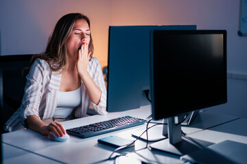 Woman yawning at her desk while working late at night