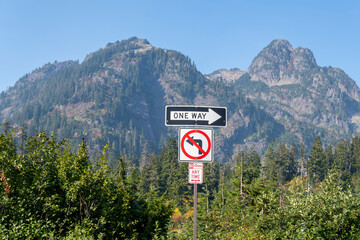 Road signs: One way, No parking any time, forbidden left turn, on the mountain background