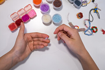 The girl's hands are weaving a beaded bracelet. Development of creative abilities in children. View from above.