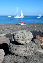 Lava stones, pebbles stacked in a pyramid on the beach, sea with boat in the background, Stromboli...
