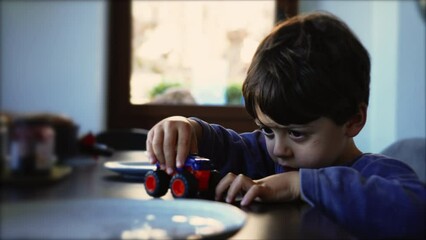 Child plays with car toy by himself. Creative little boy playing in the morning table wearing pajamas