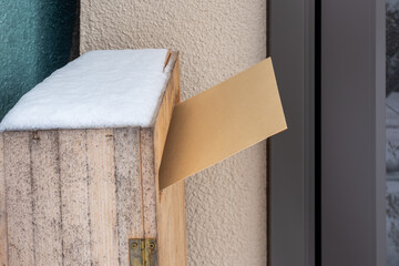 雪の日の玄関横の木製のポストに投函された大型の茶封筒