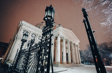 Winter night in Bucharest. Romanian Atheneum landmark building under snowfall during a winter...