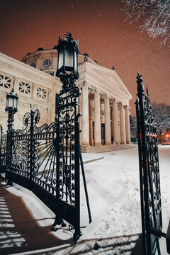 Winter Night In Bucharest. Romanian Atheneum Landmark Building Under Snowfall During A Winter Evening In Bucharest, Romania. Wide Angle View Through The Iron Gate.