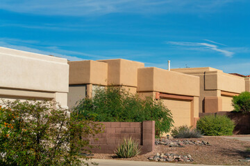 Row of adobe cement houses in late afternoon sun with rock gardens and trees in front yard in late afternoon sun