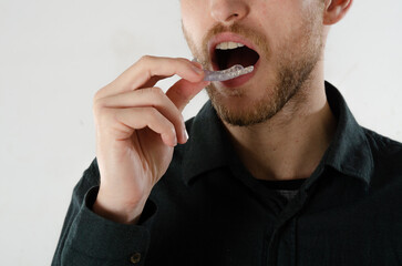 Man taking off transparent silicone aligner for orthodontics. Concept of dentist, orthodontic treatment and pretty smile. Background isolated on white background