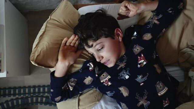 Preteen young boy lying in bed waking up. Kid waking up