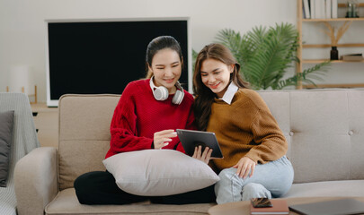 Two asian students learning together online with a laptop, tablet and tutor together in liveing room