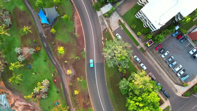 Drone aerial of blue teal retro car  down long winding road along coastline. Beach waves crashing. Past residential neighbourhood, Nightcliff jetty. Birds eye view. Thunderbird car