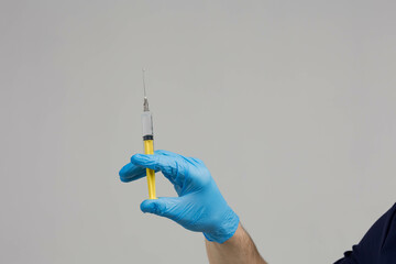 Closeup doctor's hand in rubber glove holding transparent syringe without cap with vaccine on light...