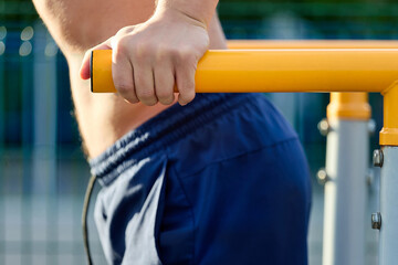 Close-up of a man in sports shorts doing push-ups on parallel bars at an outdoor stadium. A strong...
