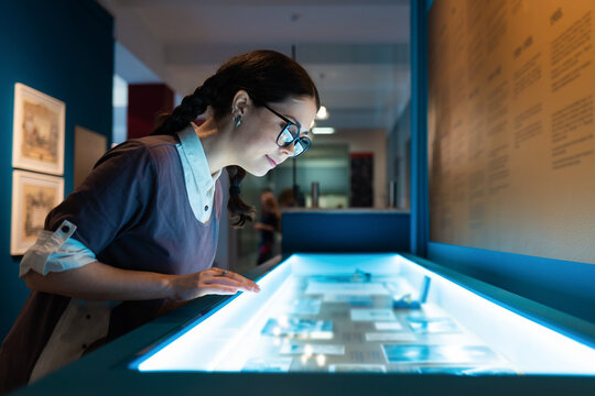 Cultural education and excursion. Side view of caucasian pretty young woman wearing glasses contemplates exhibition. Electric blue light
