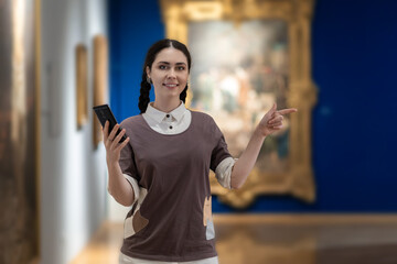 Portrait of young Caucasian woman using smartphone and point to right side. Visiting gallery or...