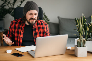 Young man is a freelancer in casual clothing, he concentrates on a laptop in a cafe. A stylish young man looks at the laptop screen with amazement. Work on a laptop in a cafe