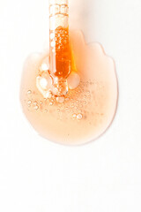 Cosmetic dropper pipette with drops of product on the whte background of golden smear with bubles.