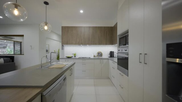 Contemporary open plan kitchen, island bench and breakfast area. White finishes. Large modern kitchen stove and oven. Clean crisp home. white tile plash back. Stone bench top. Pendant lights