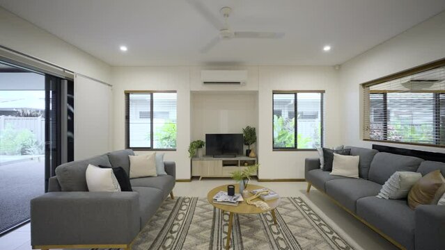 Contemporary open plan living room. White finishes in a white house. Clean crisp home. Styled with TV units, couches, tables and rug. Sliding door to outdoor area. Modern split system aircon