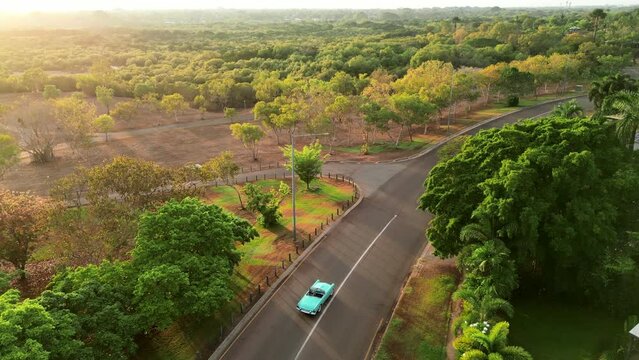 Drone aerial of blue teal retro car  down long winding road to river. Native Australian green trees skyline. Sunset
Thunderbird