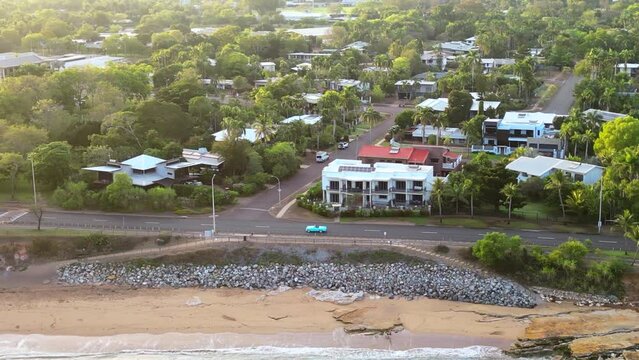 Drone aerial of blue teal retro car  down long winding road along beach coastline. Past residential neighbourhood, Nightcliff jetty. Native Australian green trees skyline. Sunset. Thunderbird car