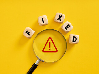 To fix an error or system bug. The word fixed on wooden cubes with a magnifier on a warning symbol.