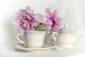 Fototapeta na wymiar Set of antique porcelain coffee cup with sugar bowl and gorgeous pink peonies in a vase on a white background