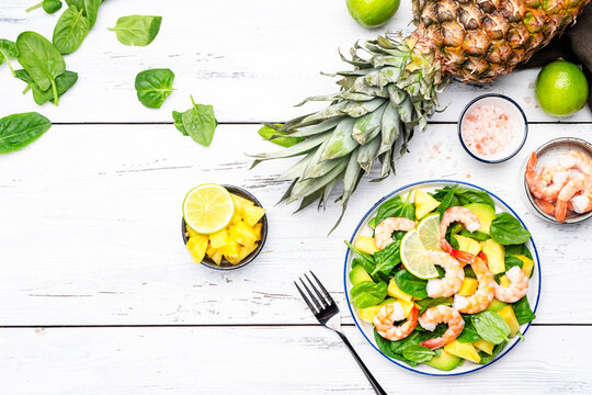 Shrimp pineapple salad with spinach, avocado and lime on white wooden table background, top view. Healthy vegetarian eating, balanced, clean diet food, weight loss dish