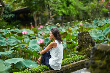 A young, beautiful woman is resting by the lotus pond. Portrait of a beautiful woman in a green...