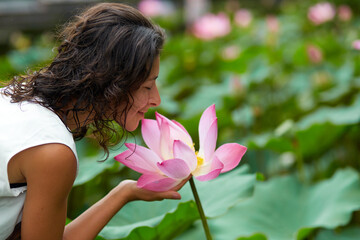 Obraz na płótnie Canvas A young, beautiful woman is resting by the lotus pond. Portrait of a beautiful woman in a green park by a lotus pond with blooming lotuses