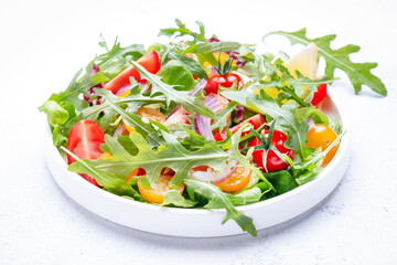 Fresh spring vegan vegetables salad with colorful cherry tomatoes, cucumber, red onion, lettuce, radicchio and arugula. White table background, top view