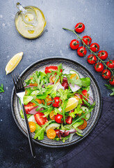 Fresh spring vegan vegetables salad with colorful cherry tomatoes, cucumber, red onion, lettuce, radicchio and arugula. Dark table background, top view