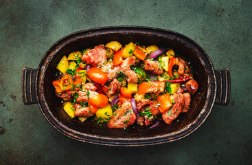 Turkey drumsticks roast with potatoes, paprika, onions, herbs and spices in rustic cast iron pan, old green table background, top view