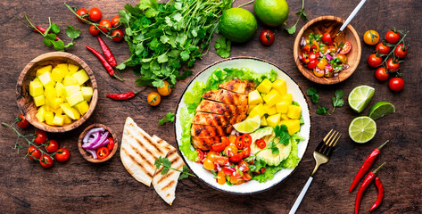 Grilled chicken salad with avocado, mango, tomato salsa, cilantro and lettuce in mexican style,...