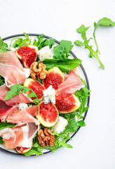 Fresh fig salad with prosciutto, gorgonzola, walnuts, arugula on white kitchen table background, top view, copy space