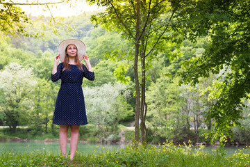 the girl in the blue dress ,a white hat on a background of the river ,with the dreamy eyes