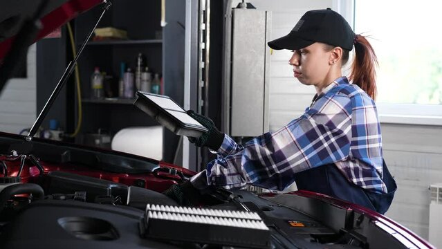 Caucasian female auto mechanic changes the engine air filter in the car.
