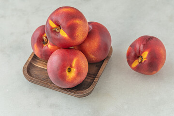 Fototapeta na wymiar ripe sweet nectarines on a wooden plate on white marble surface