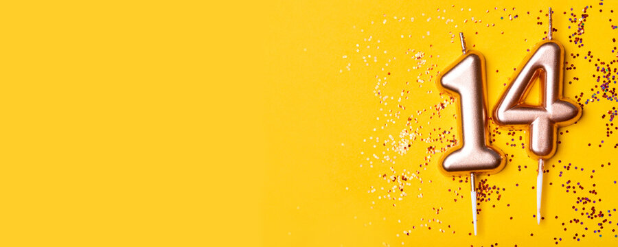 Gold candles in the form of number fourteen on yellow background with confetti. 14 years celebration.