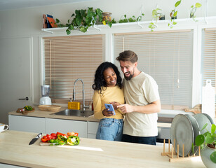 Young heterosexual diverse couple looking at mobile in a kitchen