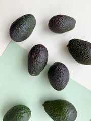 Many tasty ripe avocados on light green background, flat lay