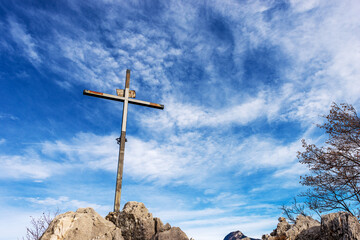 Metal religious cross on the top of a mountain peak against a blue sky with clouds and copy space....