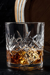 Whiskey in a glass with a barrel. Bourbon whisky and a cask on a dark background, a close-up of the classic luxury drink
