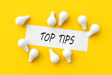 The word top tips on white paper surrounded with light bulbs. Useful advice, information or ideas...