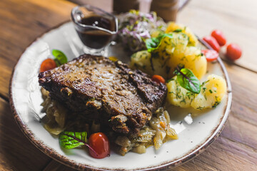 Close-up of pork ribs with boiled potatoes and gravy decorated with cherry tomatoes served on white plate. Restaurant dish. Polish cuisine. Horizontal indoor shot. High quality photo