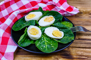 Spinach leaves and halved boiled eggs on a black plate