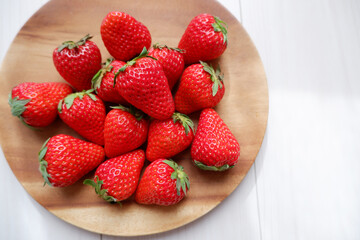Fresh strawberries on wooden plate. ripe red strawberries on white wooden background. Fresh seasonal fruits. 